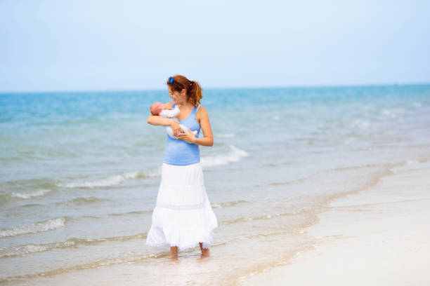 Mother and newborn child walking on beautiful beach. First vacation with baby. Travel with infant kid. Active fit mom after birth. Summer holiday family fun.