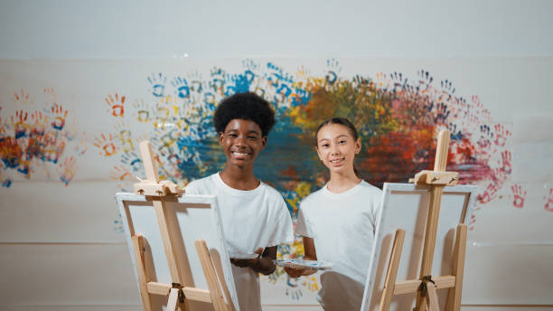 istock African boy and caucasian girl look at camera while paint canvas. Edification. 2157930655