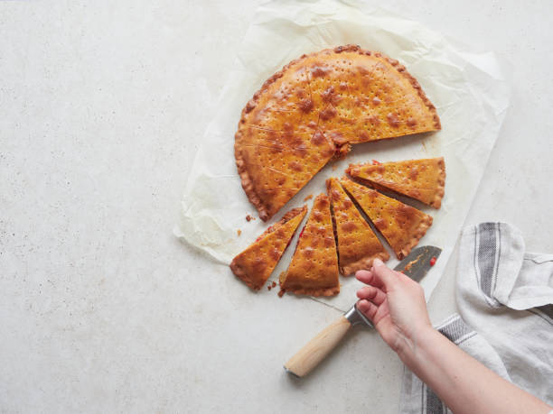 istock Seen from above woman's hand picking a triangular piece of dough with vegetable filling freshly baked called empanada on white paper, knife and kitchen towel on the table. 2157930779