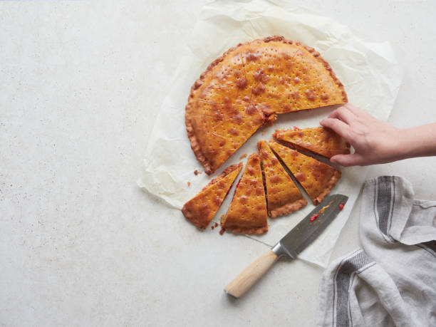 istock woman's hand picking a triangular piece of dough with vegetable filling freshly baked called empanada on white paper, knife and kitchen towel on the table. 2157930780