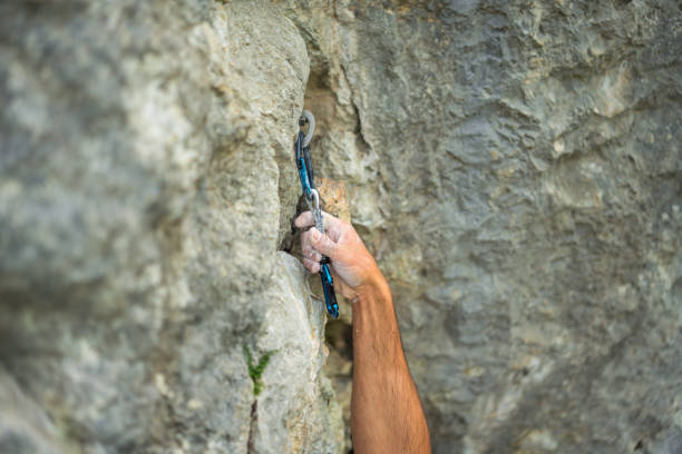 A determined man scales a steep crag, securely clipping a carabiner for safety while dressed in climbing attire, showcasing strength and focus outdoors.
