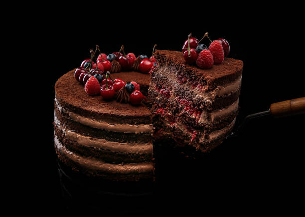Sliced chocolate cake with fruit filling decorated with raspberries, cherries and blueberries on a black background