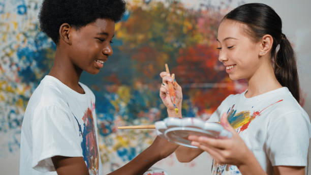 istock Smiling diverse children paint color on each other shirt at wall. Edification. 2157933434
