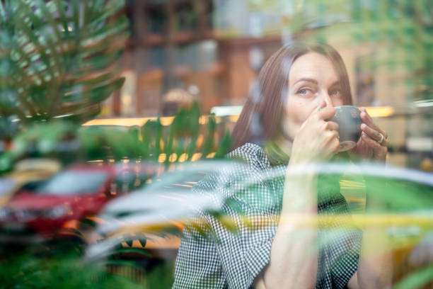 istock Beautiful woman sits at cafe, drinking coffee and looking through window 2157933545