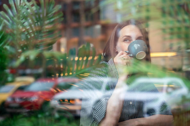 istock Beautiful woman sits at cafe, drinking coffee and looking through window 2157933567