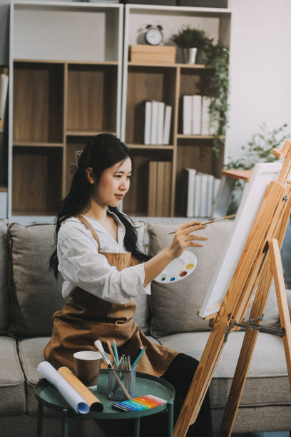Pretty talented female painter painting on easel, making colorful sketches, creating marine landscape. Beautiful female artist painting with watercolor paints. Creativity and imagination concept