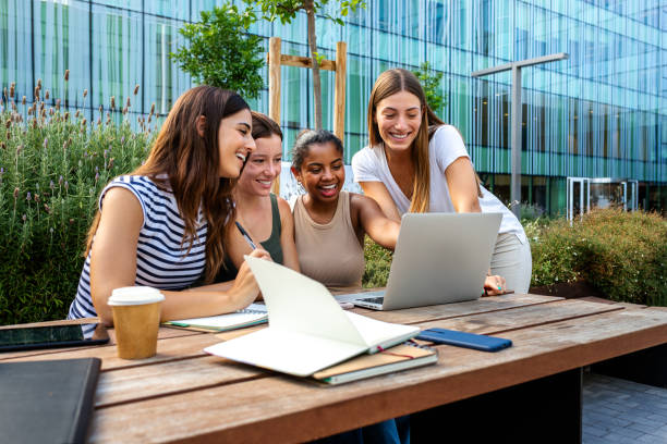 istock Young female black university student doing homework with friends outdoors in college campus using laptops. 2157938447