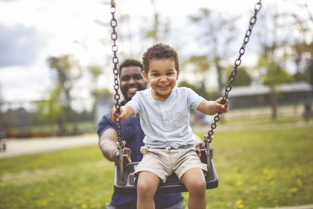 playtime moments. father with her son swinging having fun on the playground outside, sharing laughter and joyful bonding in park outdoors - kinderspielplatz stock-fotos und bilder