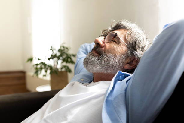 Mature man relaxing at home sitting on the sofa with hands behind the head feeling satisfaction. Copy space