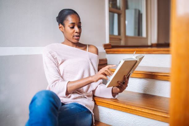 istock Black woman sitting on a staircase and reading a book 2157948055