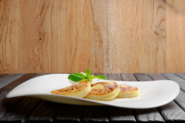 Sprinkling sugar powder from above on cottage cheese fritters