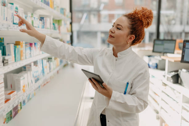 istock Pharmacist pointing at medicine shelf with tablet 2157952078