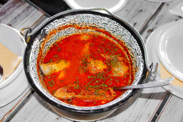 Fish stew in a traditional cauldron on a wooden table spiced with parsley and crushed paprika.