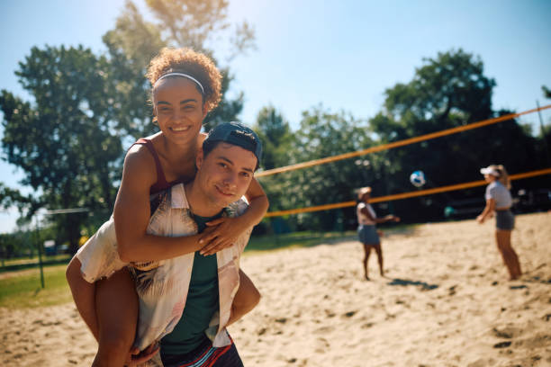 istock Happy couple piggybacking while playing beach volleyball and looking at camera. 2157966116