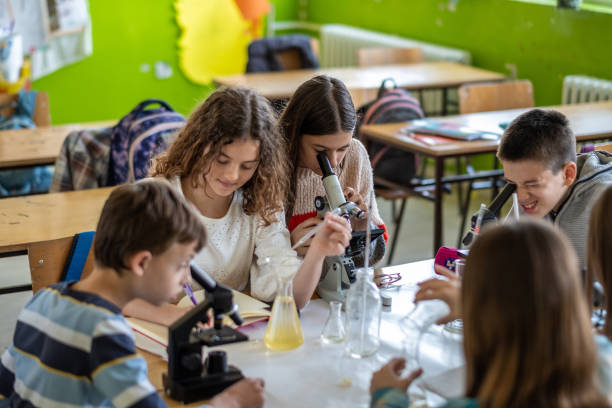 teenagers at school learning about chemistry, mixing chemicals, sitting on benches together, in the classroom, laughing, studying, researching, reading, microscope