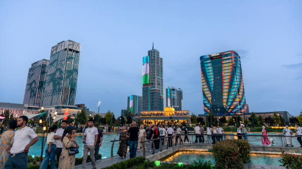 Tashkent, Uzbekistan. May 15th, 2024. People walking on the bridge over the pond at the new public park in the city, with the country’s tallest building to date  illuminated in the background.