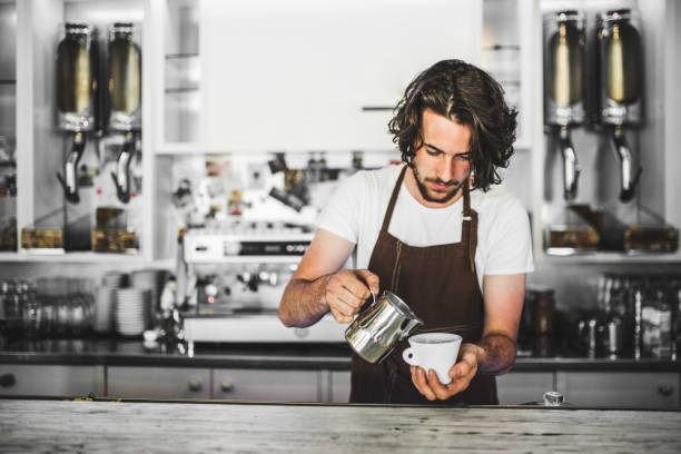 Handsome barista working in coffee shop, preparing coffee. University student working part-time in cafe.