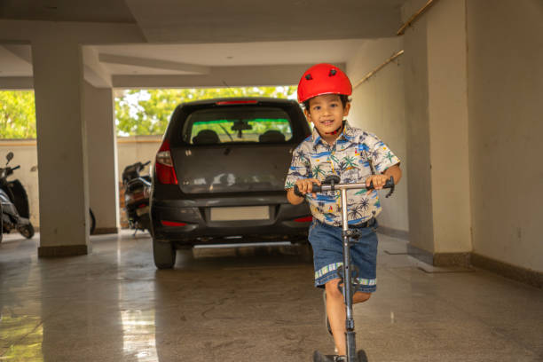 Portrait of cute boy wearing red helmet and riding push scooter in parking lot during weekend