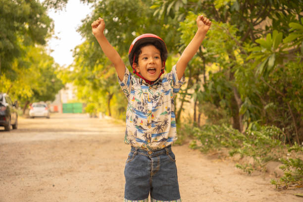 Young boy stands barefoot on a wooden pier, rising arms in rock on gesture. . Dressed in a striped t-shirt and green shorts, he looks at the the vast, turquoise-colored sea. \nShot with Nikon D800