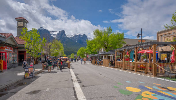 Canmore, Alberta, Canada – June 16, 2024:  People enjoy Main Street in the downtown with Mount Rundle in the Background
