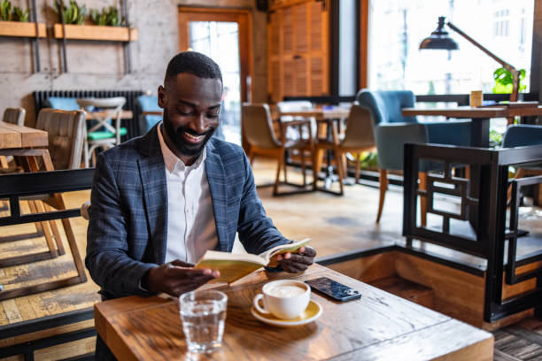 istock A young black man, a business man, elegantly dressed, reads a book in a cafe 2157995037