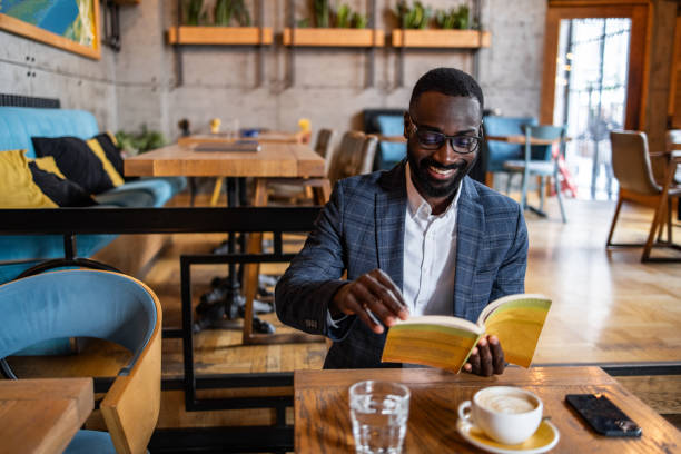istock A young black man, a business man, elegantly dressed, reads a book in a cafe 2157995053