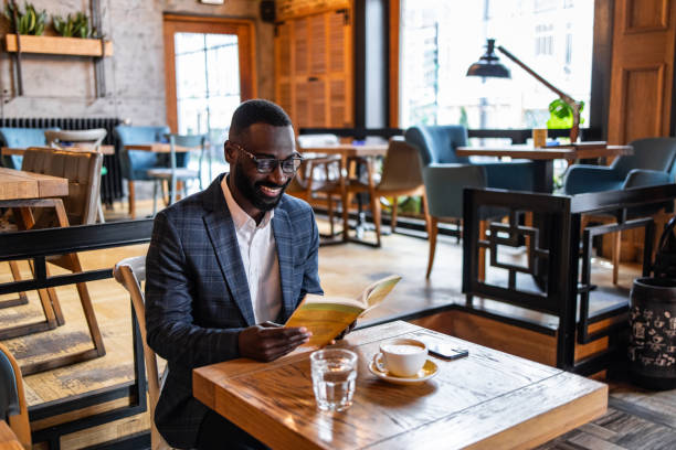 istock A young black man, a business man, elegantly dressed, reads a book in a cafe 2157995056