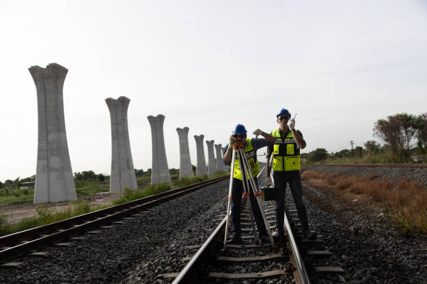 istock Two male railway technicians using theodolite surveying optical instruments and a coworker holding a blueprint  for measuring at construction rails road train tracks 2157995263