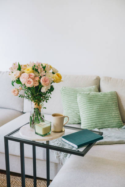istock Coffee cup, flowers, and notebook on a glass table next to a couch 2157997330