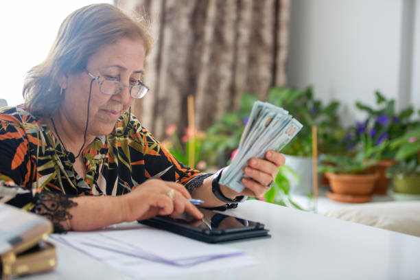 istock Senior Woman Counting  One Hundred Dollars And Doing Finances At Home 2157997554