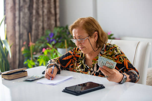 istock Senior Woman Counting  One Hundred Dollars And Doing Finances At Home 2157997676