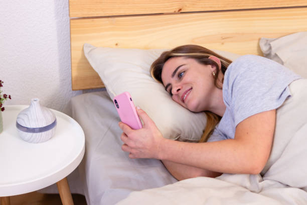 istock Young woman lying in bed is using smartphone in the morning 2157999821