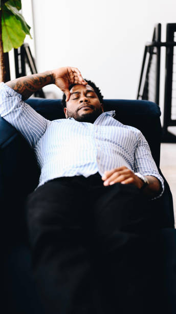 istock Young Black man laying down on a sofa at home stressed out, burnt out, tired and feeling exhausted and vulnerable 2158003722
