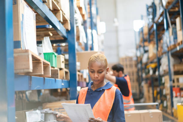istock Young woman worker checking inventory with checklist in large warehouse 2158009612