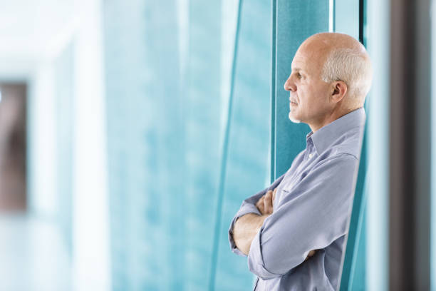 istock Senior businessman looking through office window with arms cross 2158012413