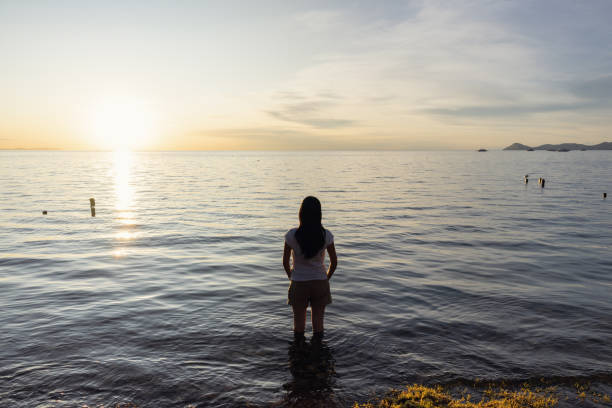 a woman looking at the sunset on the lake, with her hands in her pockets