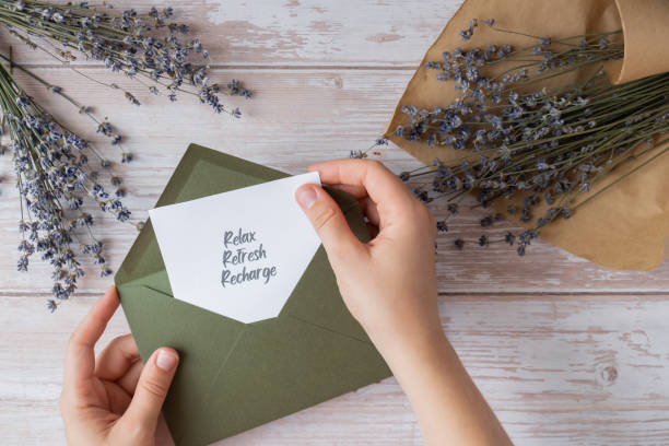 istock Female hands taking paper card note with text RELAX REFRESH RECHARGE from green envelope. Lavender flower. Top view, flat lay. Concept of mental spiritual health self care 2158025808