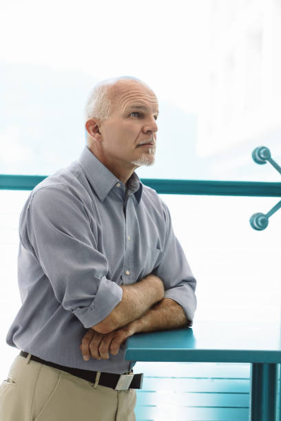 Bald man leaning, arms crossed, turquoise railing