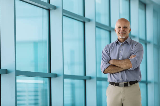 istock Senior businessman smiling with folded arms in modern office bui 2158026267