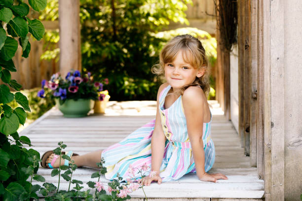 A beautiful little girl, six years old, smiles at the camera as she sits on a porch in a garden.