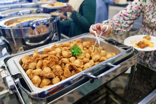 A cropped image captures businesspeople in line, using serving spoons to pick their food from the buffet.