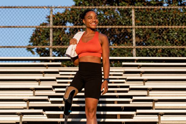 Woman athlete with prosthetic leg smiling carrying a towel standing