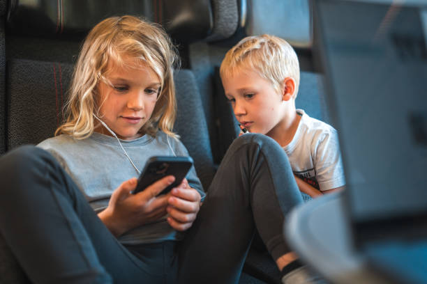 Brothers, both Caucasian, share a smartphone during their train journey in Denmark.