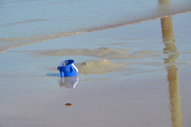 An abandoned shark bucket rests at the water's edge on Ponce Inlet Beach in Florida, with waves looming as the bucket is gradually buried in the sand.
