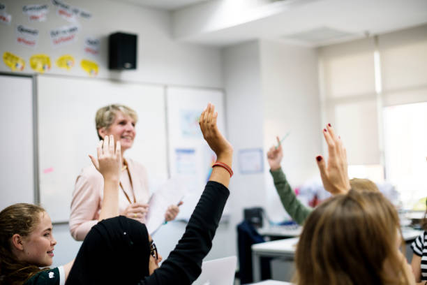 istock Students with their hands up responding to their teacher 2158050821
