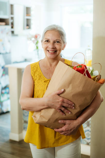 istock Senior Woman Smiling with Grocery Bag in Kitchen 2158055240