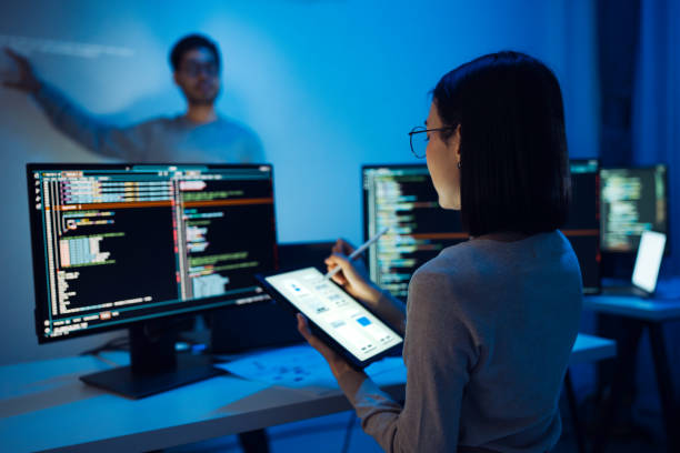istock UX designer works on a tablet while a colleague tests  application in the background in office 2158058836