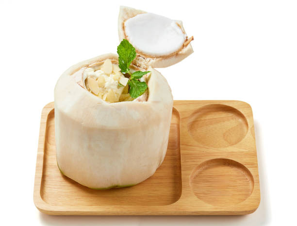 Coconut ice cream scoop into fresh coconut shell top with mint leaves and nuts placed on a wooden tray isolated on white background. Creamy white ice cream with sweet flavor. Very popular in Thailand.