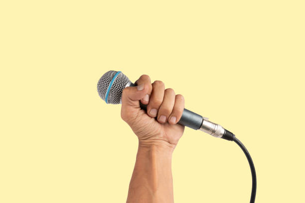 istock Black male hand holding a microphone isolated on light yellow background 2158069065