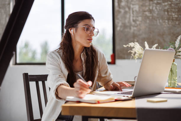 istock Freelancer in wireless earphone using laptop near notebooks on table at home 2158070862
